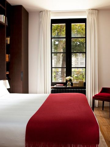Helles Schlafzimmer mit roten Details und großen Fenstern mit Blick ins Grüne.