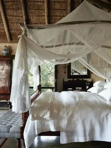 Lodge-Suite mit Himmelbett und elegantem Interieur, überdachtes Strohdach.