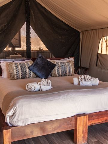 Doppelbett mit hellen Decken und Kissen im Inneren eines Wilderness Tents mit Holzboden