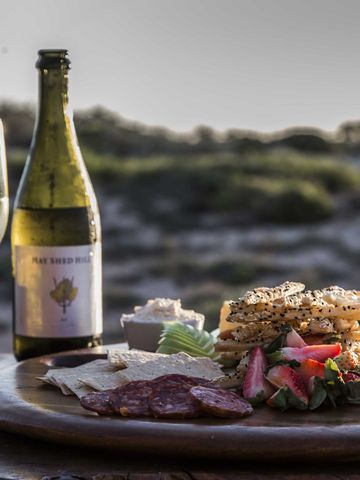 Zwei Gläser Sekt, eine Flasche und eine Platte mit Käse und Wurst auf einem Tisch in den Dünen