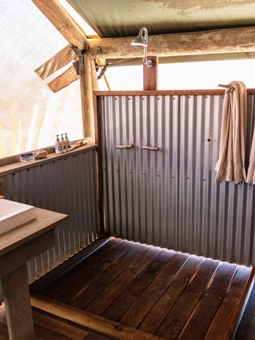 Bad eines Safarizelts mit Waschbecken auf Holzkonsole, Spiegel, Wellblechwand und Handtüchern