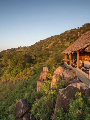 Bungalow mit traditionellem Grasdach auf Felsen mit Blick auf Serengeti