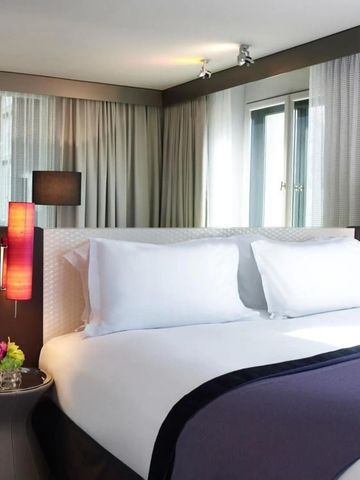 Komfortables Doppelbett in einem hellen Zimmer des Sofitel Munich Bayerpost.