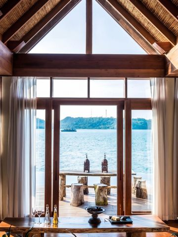 Blick aus einer Villa mit Holzdecke auf das Meer und eine Terrasse mit rustikalen Möbeln