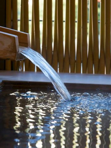 Wasser fließt aus einem Holzauslauf in ein entspannendes Thermalbad.