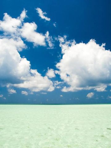Klarer blauer Himmel mit großen weißen Wolken über türkisfarbenem Meer