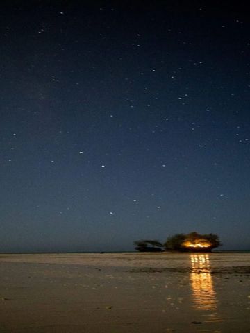 Sternenbedeckter Himmel über ruhigem Meer in der Nacht mit einem fernen Licht