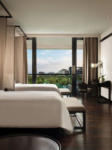 Elegantes Hotelzimmer mit zwei Betten und Poolblick durch große Fenster.