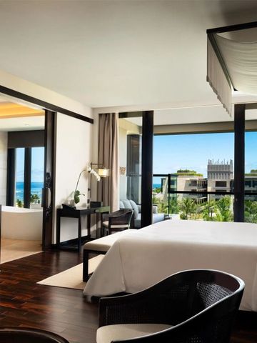 Stilvolles Zimmer mit großem Bett und Balkon mit Blick auf Garten und Meer.