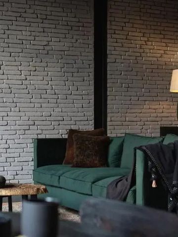 Stilvolle Lounge mit grüner Samtcouch und Backsteinwand