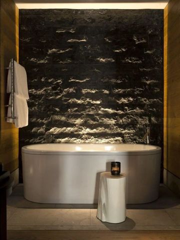 Elegantes Badezimmer mit freistehender Badewanne und Steinwand