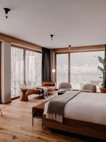 Helles Hotelzimmer mit großem Bett, Schreibtisch und Panoramafenstern zur Natur