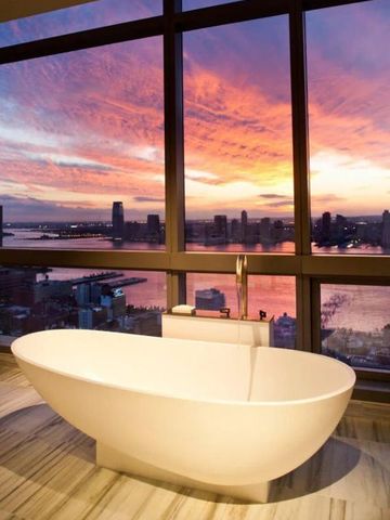 Freistehende Badewanne mit atemberaubendem Sonnenuntergang und Stadtblick.