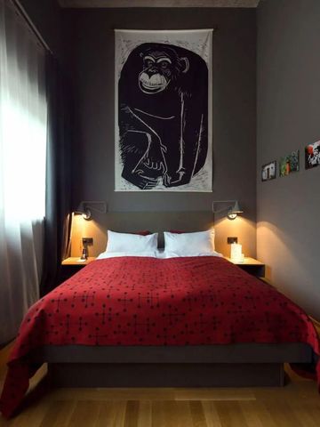 Stilvoll eingerichtetes Hotelzimmer mit roter Bettdecke und Kunst an der Wand