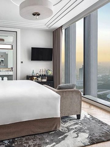 Helles Schlafzimmer mit großzügigen Fenstern und Aussicht auf die Stadt bei Sonnenuntergang.