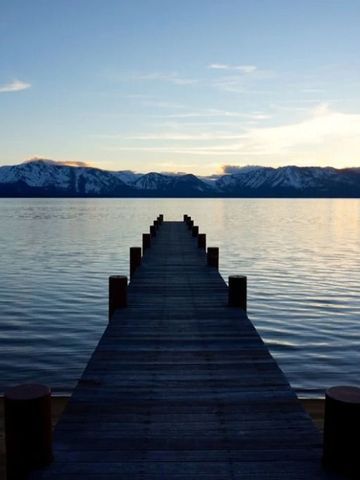 Langer Steg in einen ruhigen See bei Sonnenuntergang mit schneebedeckten Bergen im Hintergrund