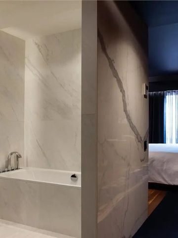 Luxuriöses Badezimmer mit Marmorwänden und blick in das Schlafzimmer.