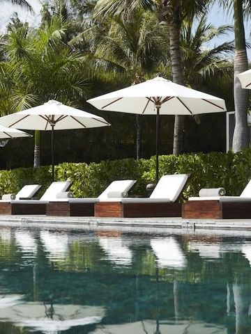 Sonnenliegen am Pool mit weißen Sonnenschirmen und Palmen im Hintergrund