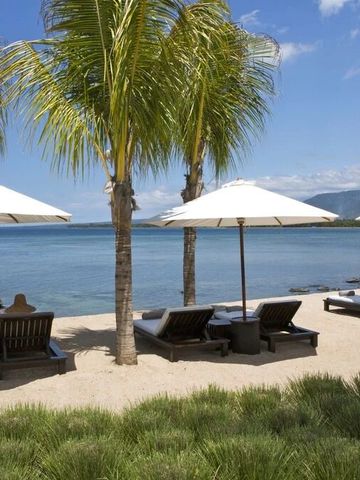 Strand mit Liegestühlen und Sonnenschirmen vor Palmen und Meerblick