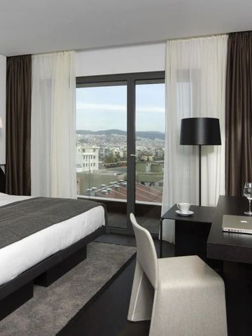 Helles Hotelzimmer mit Doppelbett, Schreibtisch und großem Fenster mit Stadtblick