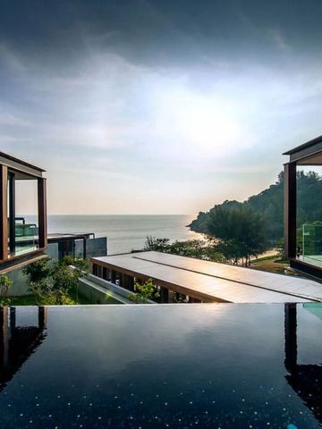 Sicht über einen glänzenden Pool auf das Meer und die umliegende Landschaft bei Sonnenuntergang in The Naka Phuket.