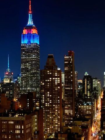 Empire State Building und umliegende Hochhäuser bei Nacht mit strahlendem Licht
