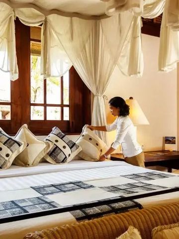 Servicemitarbeiter richtet Bett mit edlen Textilien und dekorativen Kissen her