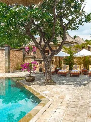 Poolbereich mit Liegestühlen umgeben von exotischen Pflanzen und traditioneller Architektur