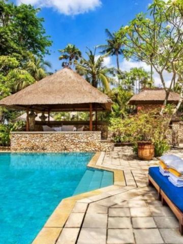 Tropische Poollandschaft mit Sonnenliegen und balinesischem Pavillon im Hintergrund