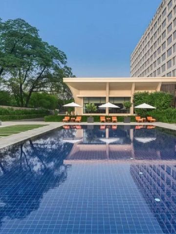 Außenpool im Oberoi New Delhi umgeben von grünen Bäumen und luxuriösen Liegen.