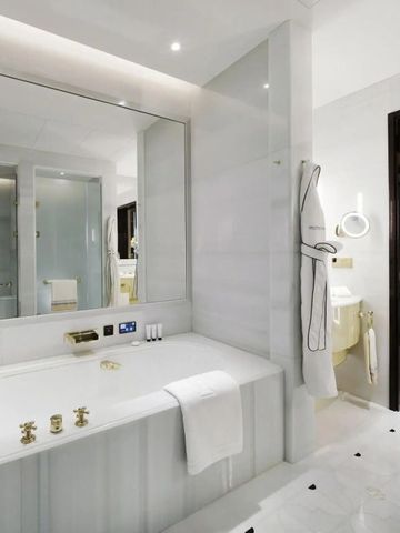 Elegantes Badezimmer mit großer Badewanne in hellem Marmor und goldenen Armaturen.