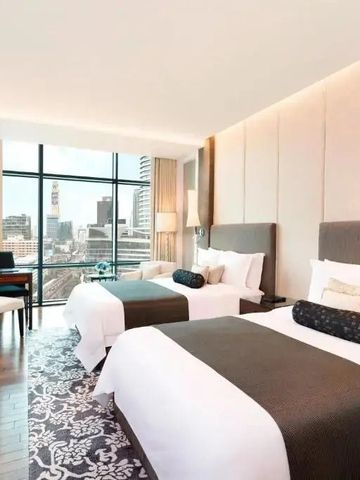 Geräumiges Hotelzimmer mit zwei Betten und Stadtblick durch große Fenster.