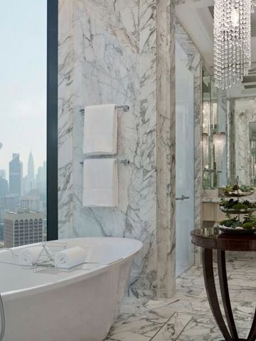 Luxuriöses Badezimmer mit freistehender Badewanne, Marmorwänden und Blick auf die Skyline.