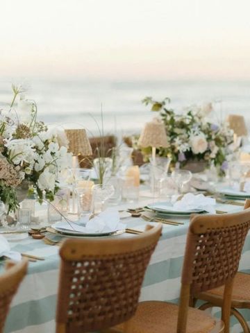 Fein gedeckter Tisch mit Blumenarrangements am Strand bei Sonnenuntergang