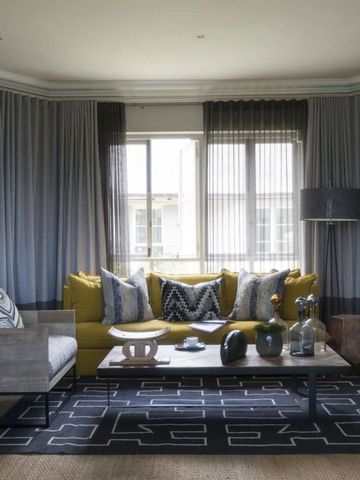 Sonnendurchflutetes Wohnzimmer mit gelbem Sofa und eleganten Vorhängen