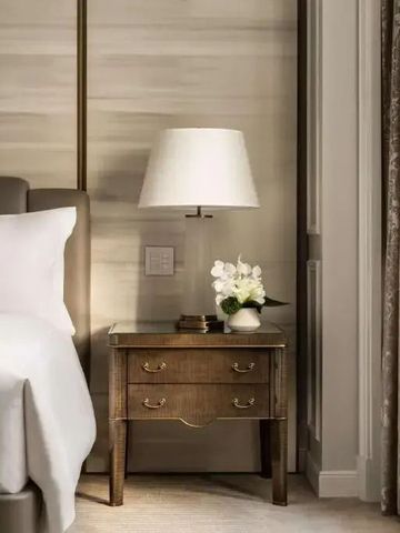 Nachttisch mit Lampe und Blumendekoration neben einem bequemen Bett