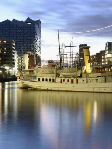 Beleuchtetes Schiff im Hafen vor moderner Architektur bei Abenddämmerung