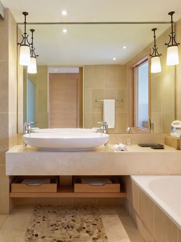 Luxuriöses Badezimmer mit großem Spiegel, modernen Leuchten und einer tiefen Badewanne.