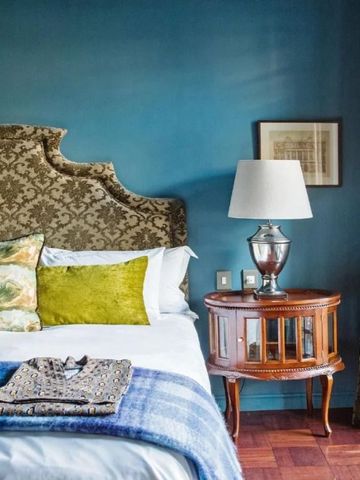 Bett in einem gemütlichen Schlafzimmer mit blauer Wand und Holz-Tisch