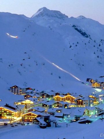 Beleuchtetes Skigebiet bei Abenddämmerung mit schneebedeckten Hütten