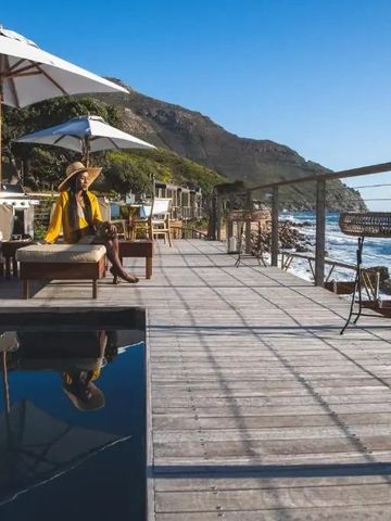 Terrasse mit Liegestühlen und Sonnenschirmen, Blick auf das Meer und die Berge.