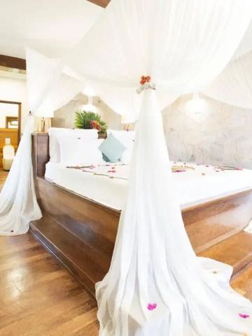 Lichtdurchflutetes Schlafzimmer mit Himmelbett und Holzboden, dekoriert mit Blüten