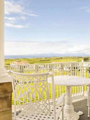 Balkon mit weißem Tisch und Blick auf grünen Golfplatz und Meer