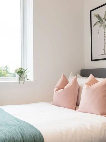 Doppelbett mit rosa Kissen und Pflanzen am Fenster