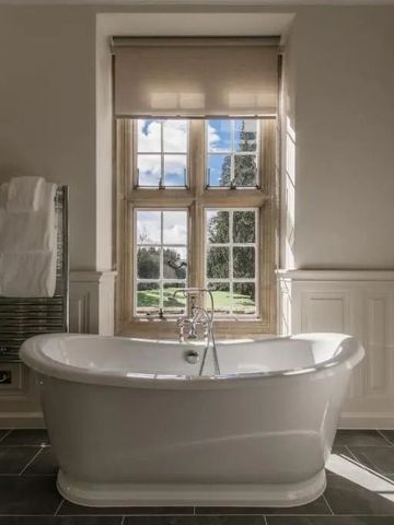 Luxuriöses Badezimmer mit freistehender Badewanne und großem Fenster mit Gartenblick