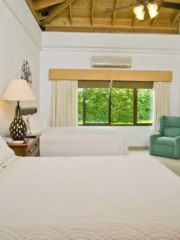 Schlafzimmer mit zwei Betten, Holzdecke und Fensteraussicht auf Pflanzen.