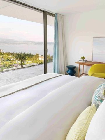 Helles Schlafzimmer mit großem Fenster und atemberaubendem Blick auf See und Landschaft