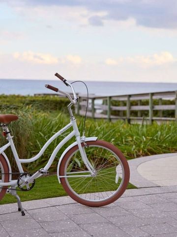 Weißes Fahrrad vor Strandstraße mit Meeresblick bei bewölktem Himmel