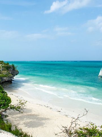 Weißer Sandstrand mit türkisfarbenem Wasser und traditionellem Segelboot.