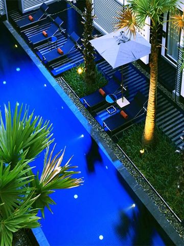 Langer blauer Pool umgeben von Palmen und Liegen